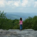 Little Girl standing on a huge rock overlooking the hills and valleys